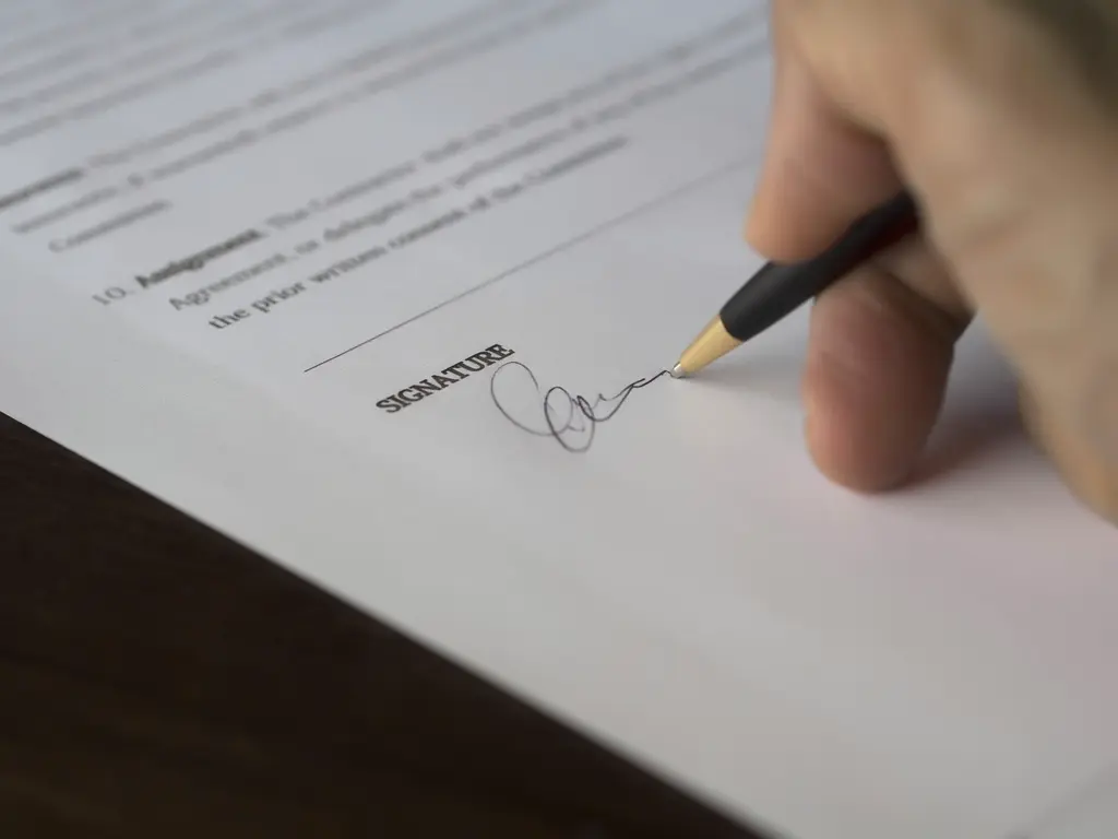 Mão assinando um contrato com caneta sobre o documento